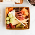 Charcuterie box filled with cheeses, meats, nuts, fruits, pickles and chocolate