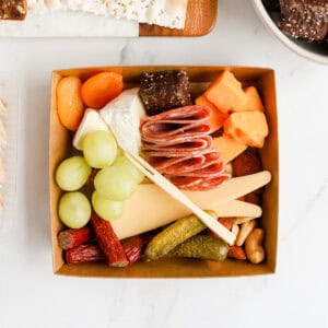 Charcuterie box filled with cheeses, meats, nuts, fruits, pickles and chocolate