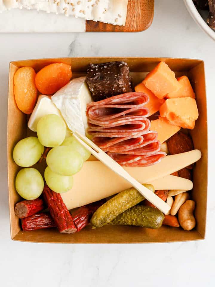Charcuterie box filled with cheeses, meats, nuts, fruits, pickles and chocolate