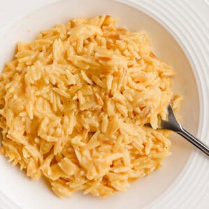Cheesy orzo served in a white shallow bowl with a fork.