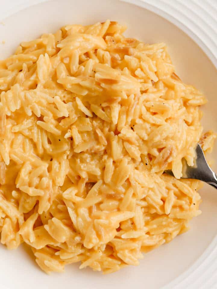 Cheesy orzo served in a white shallow bowl with a fork.