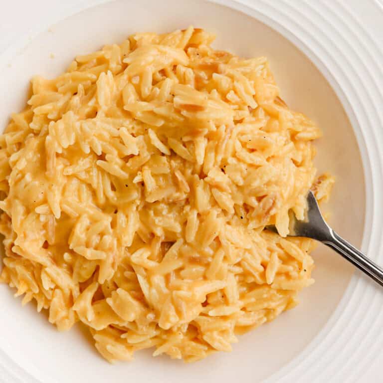 Cheesy orzo served in a white shallow bowl with a fork.