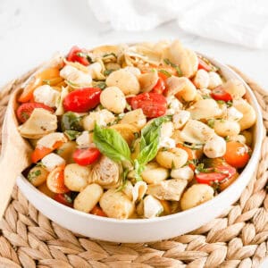 Italian gnocchi salad in a white bowl on a wicker serving tray.