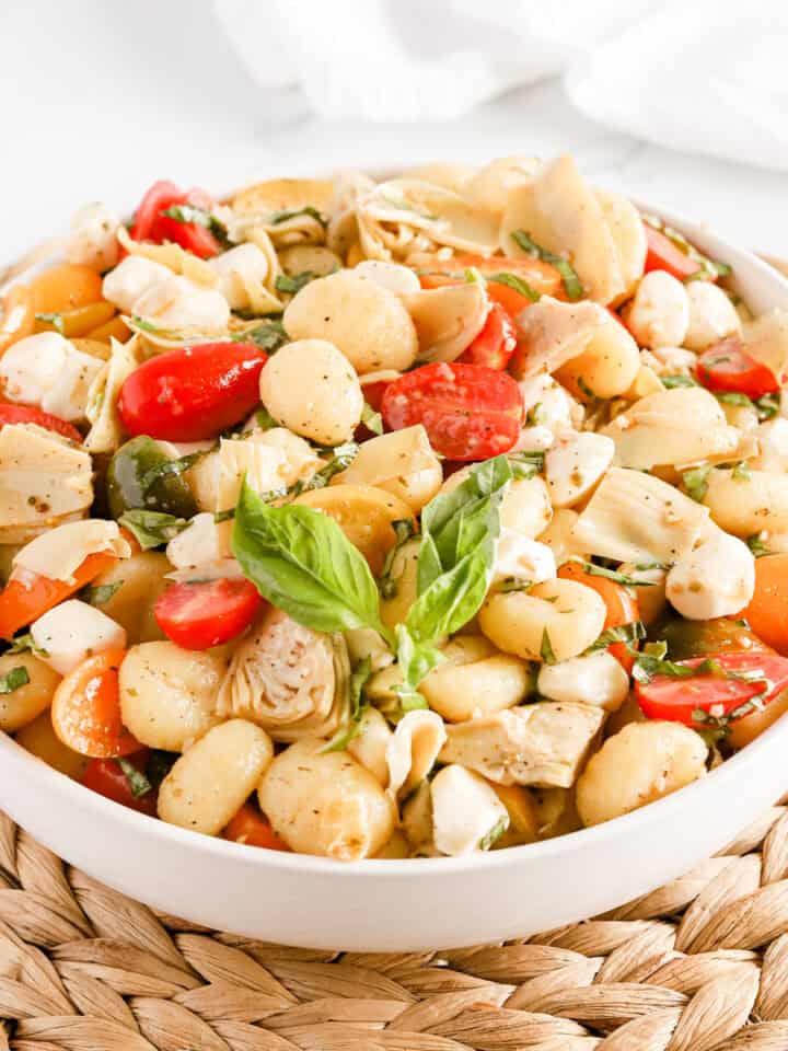 Italian gnocchi salad in a white bowl on a wicker serving tray.