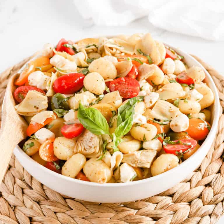 Italian gnocchi salad in a white bowl on a wicker serving tray.
