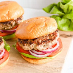 Three pork burgers on buns with lettuce, tomato and red onion.