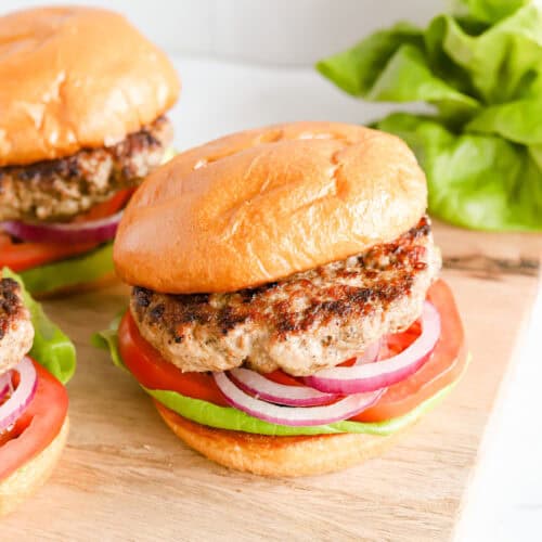 Three pork burgers on buns with lettuce, tomato and red onion.