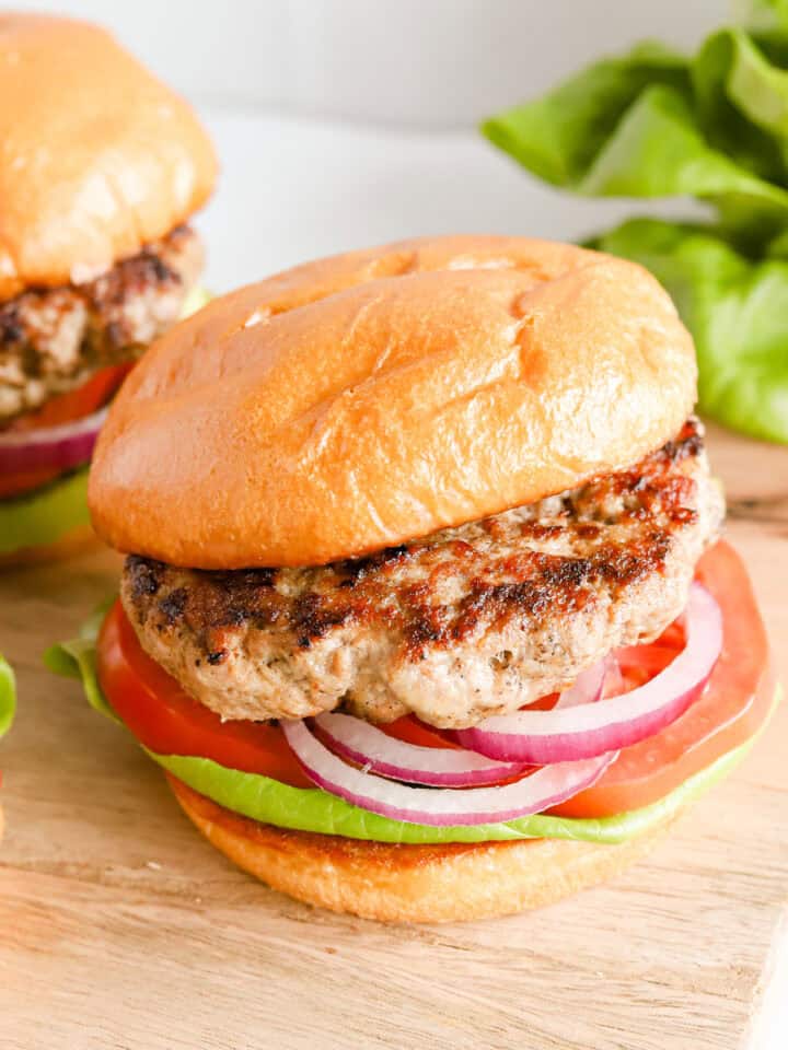Three pork burgers on buns with lettuce, tomato and red onion.