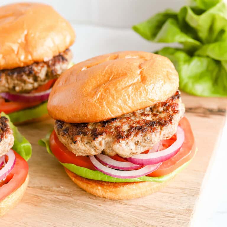 Three pork burgers on buns with lettuce, tomato and red onion.