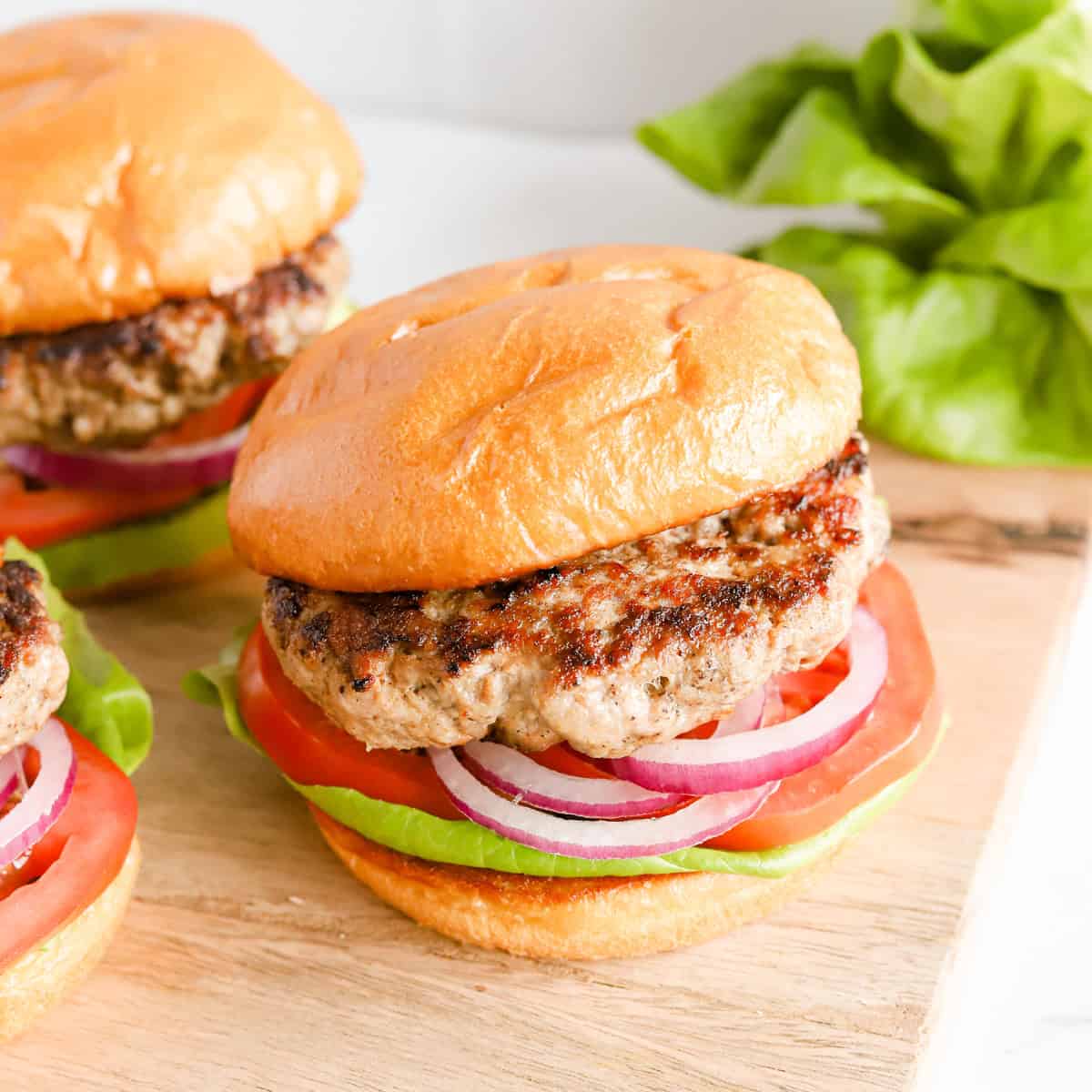 Three pork burgers on buns with lettuce, tomato and red onion.