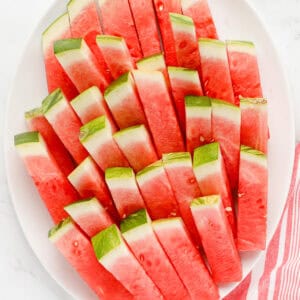 White oval platter of watermelon sticks stacked.