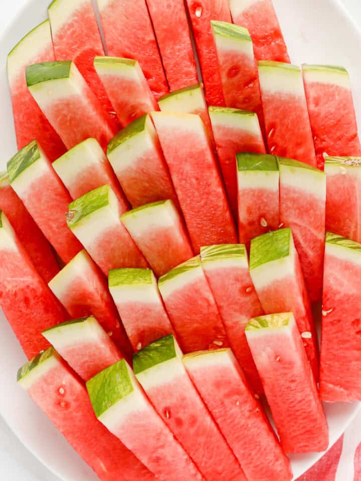 White oval platter of watermelon sticks stacked.
