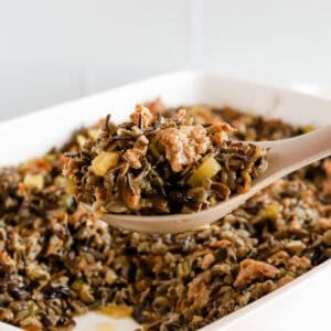 Spoonful of wild rice hot dish being lifted out of white baking dish.