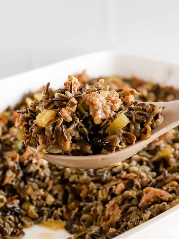 Spoonful of wild rice hot dish being lifted out of white baking dish.