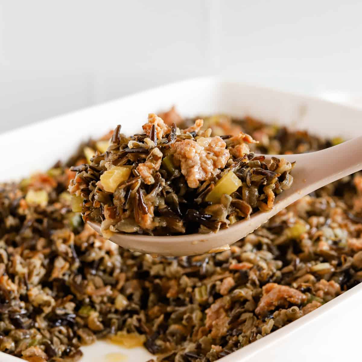 Spoonful of wild rice hot dish being lifted out of white baking dish.