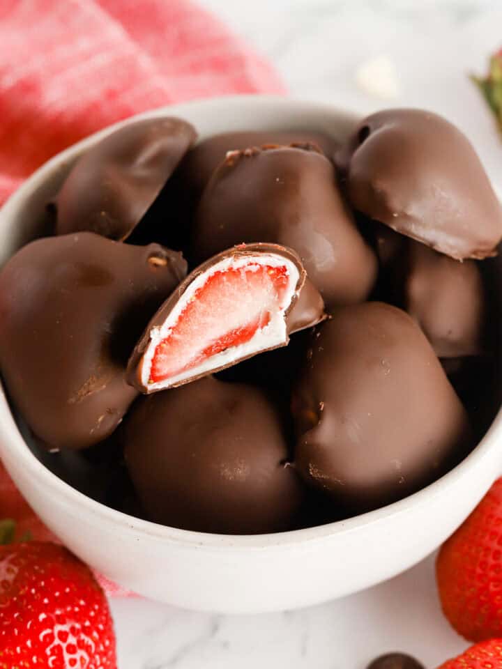 Small white bowl of dipped berries with one on top cut in half, exposing the center.