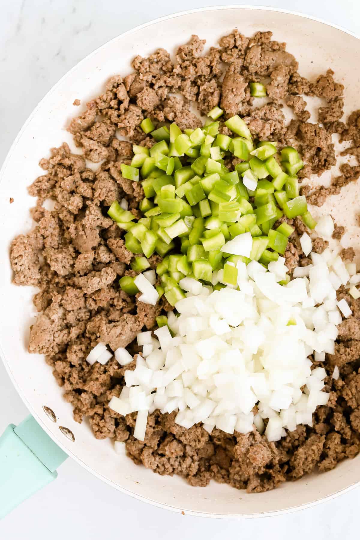 Cooked ground beef in a large skillet with chopped green peppers and onions.