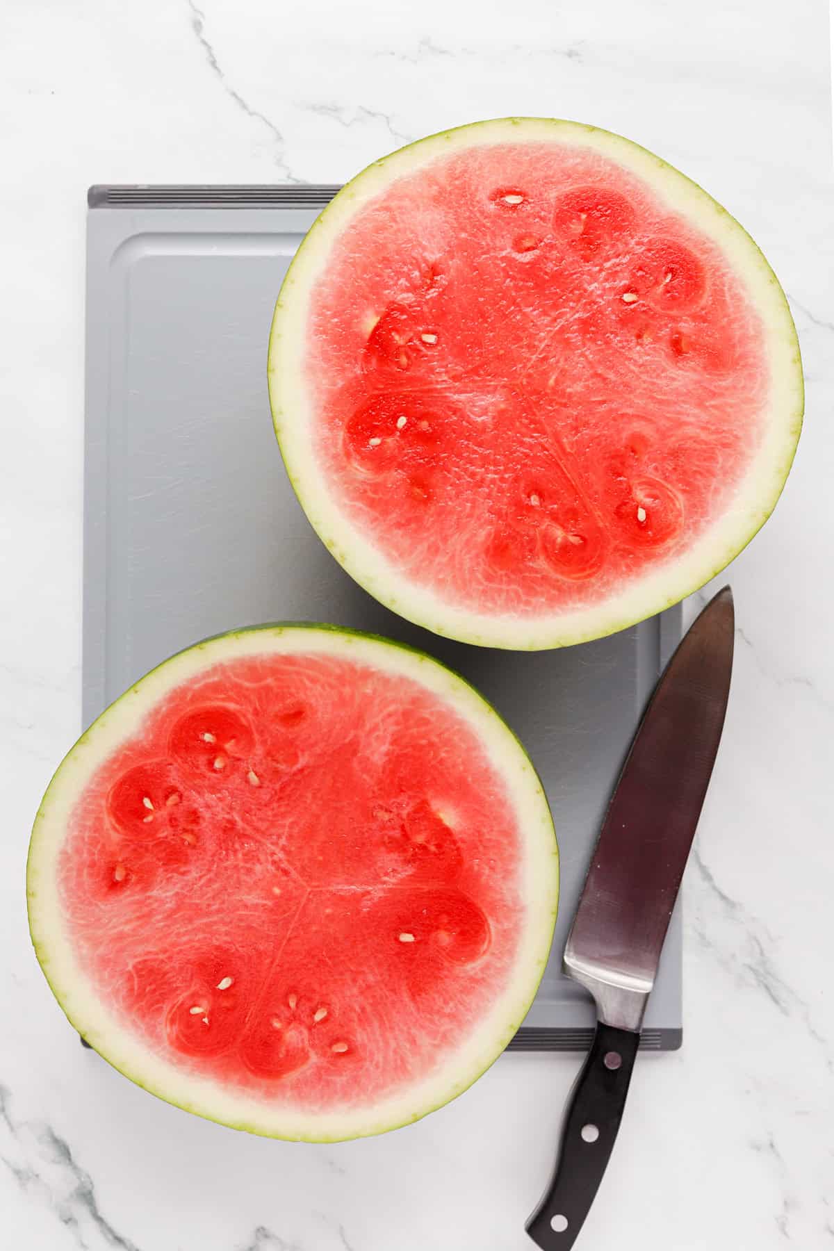Watermelon sliced in half on a cutting board with a chef's knife