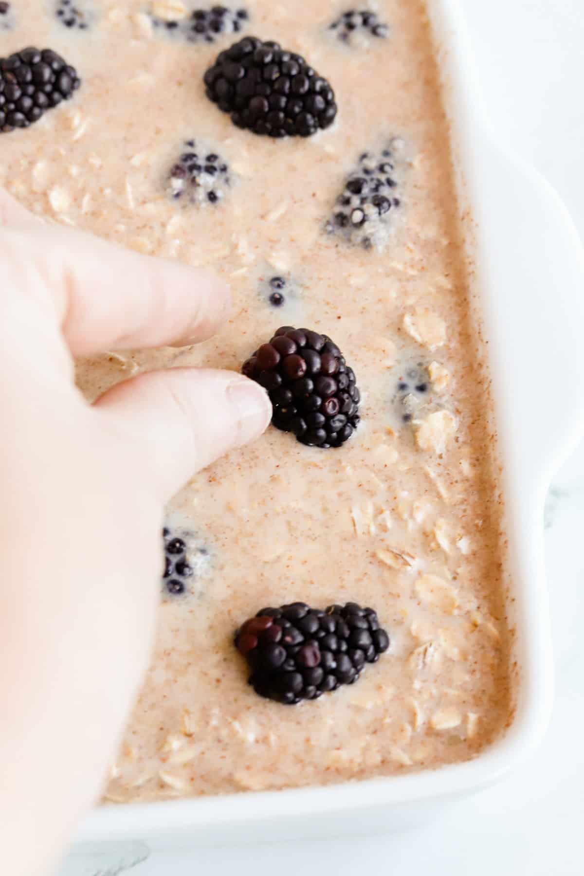 Hand placing whole blackberries on top of oatmeal batter.
