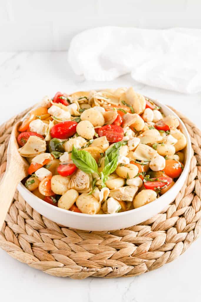 Italian gnocchi salad in a white bowl on a wicker serving tray.