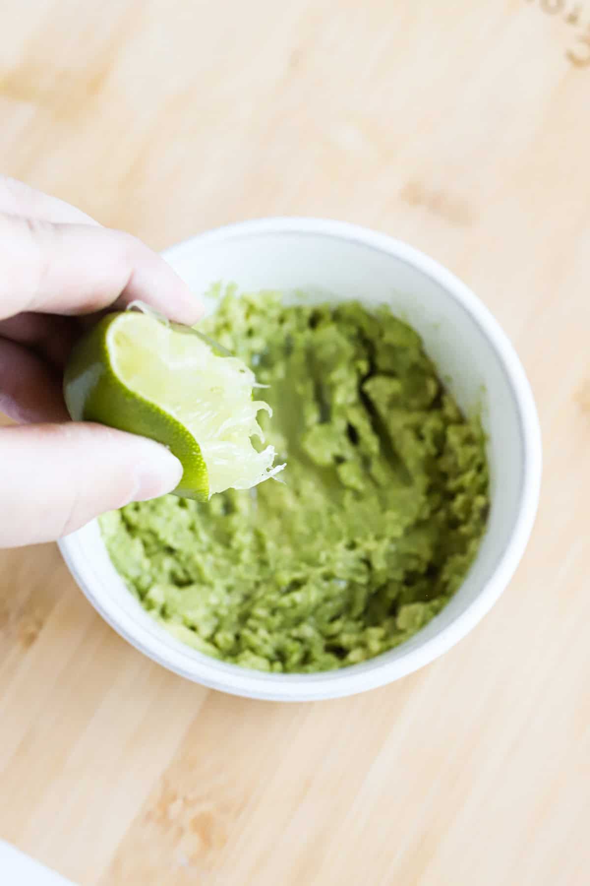 Hand squeezing half a lime into mashed avocado in a bowl