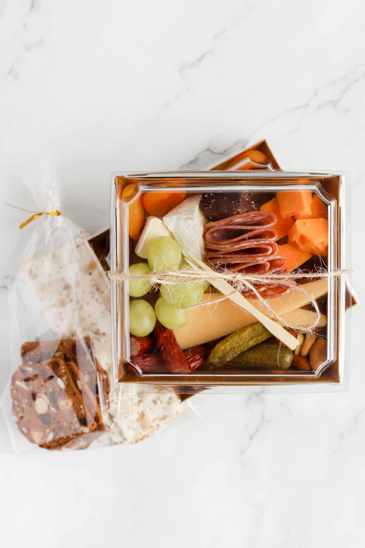 Packaged charcuterie boxes with crackers packaged in cellophane bags on the side.