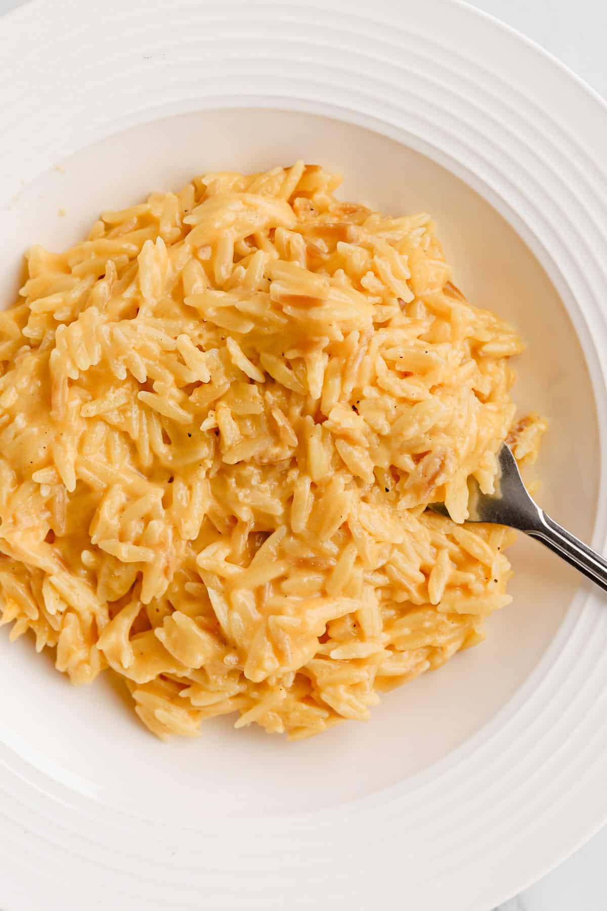 Cheesy orzo served in a white shallow bowl with a fork.