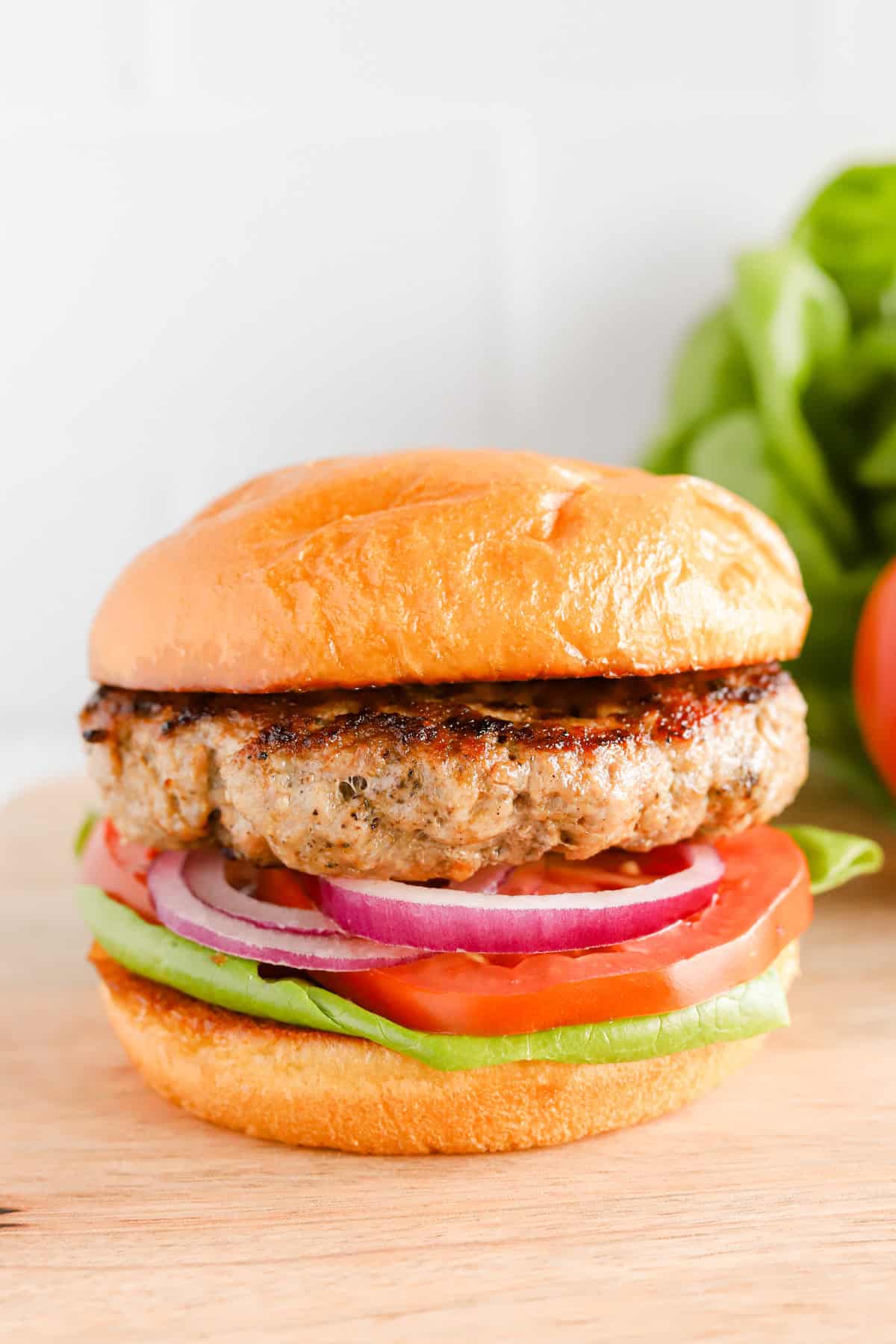 Close up of pork burger on brioche bun with red onion, sliced tomato and lettuce.