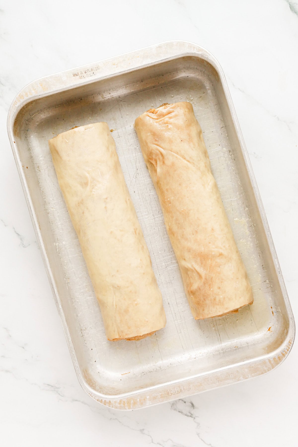 Two potica loaves rolled in melted butter in a metal 9x13 baking pan.