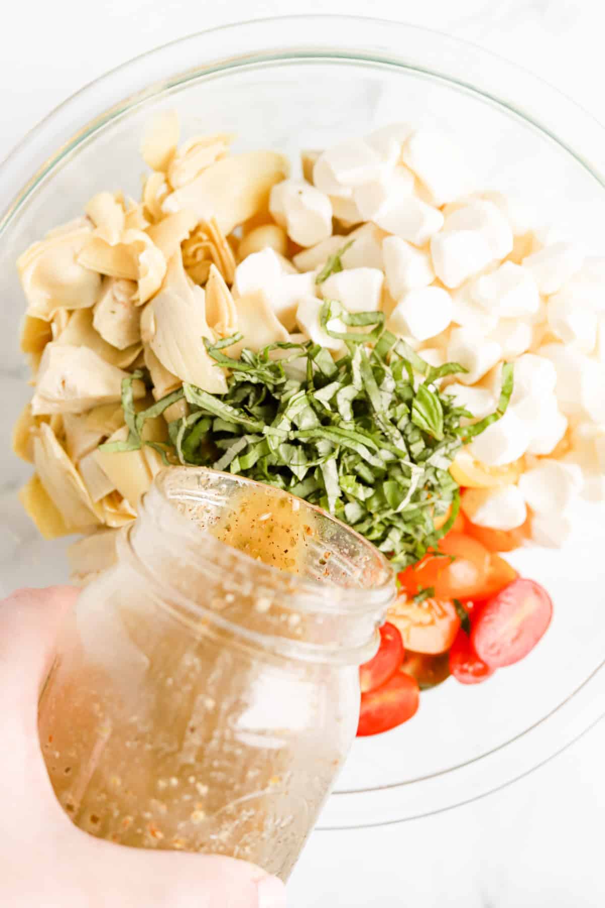 Mason jar of red wine vinaigrette being poured into gnocchi, cheese and veggies.