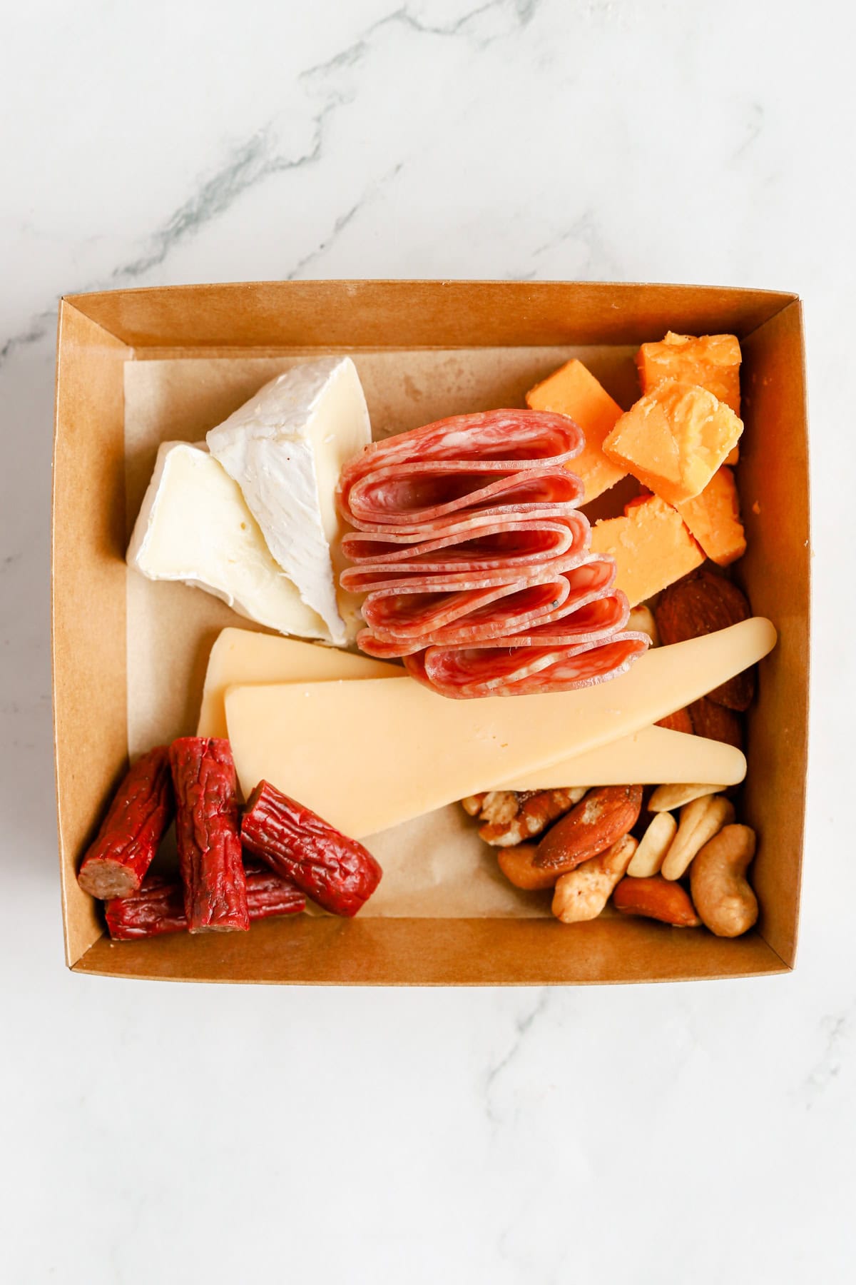 Sliced salami and cut meat sticks added to the box with cheese and nuts.