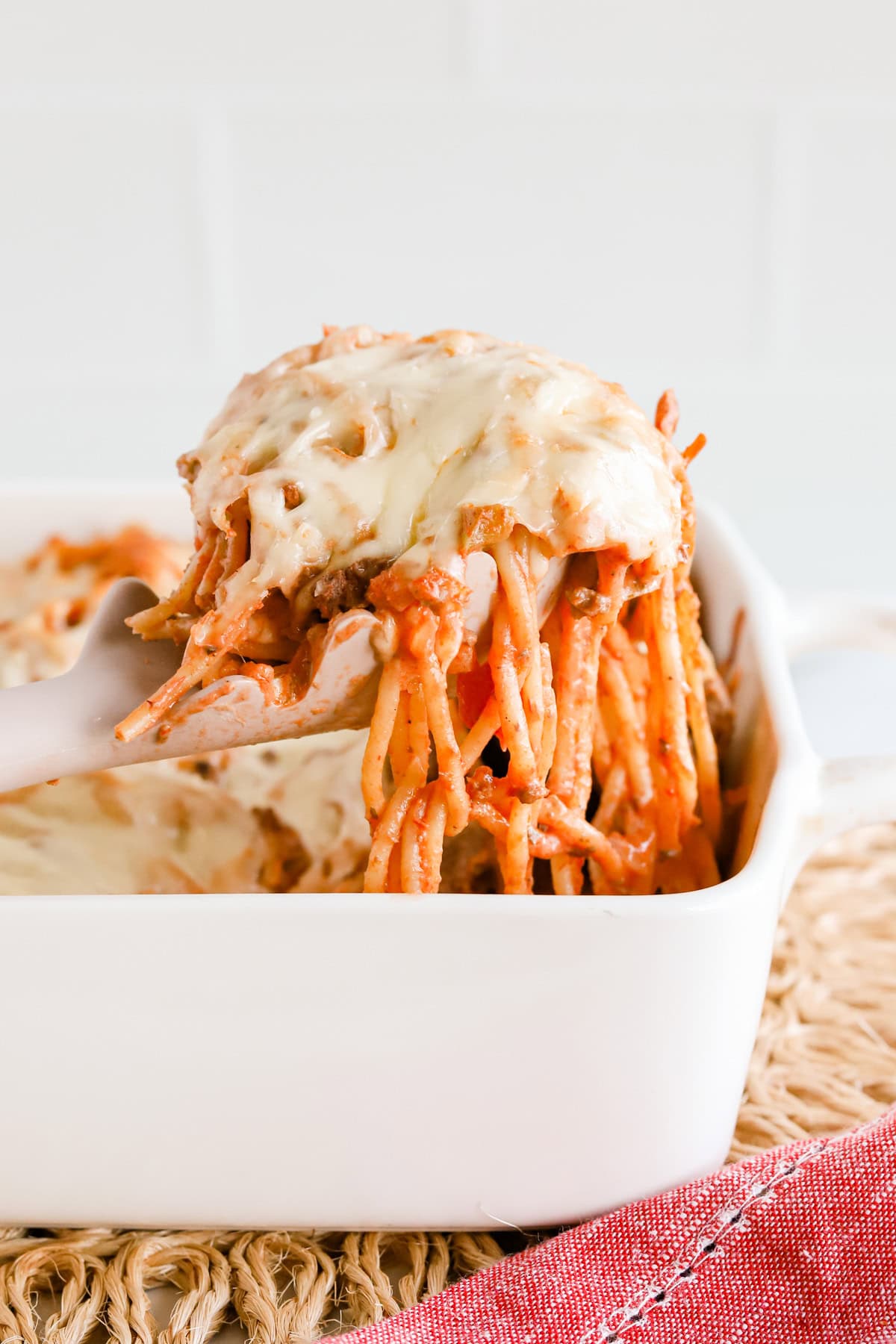 Featured image of a scoop of baked spaghetti casserole lifted out of white baking dish.