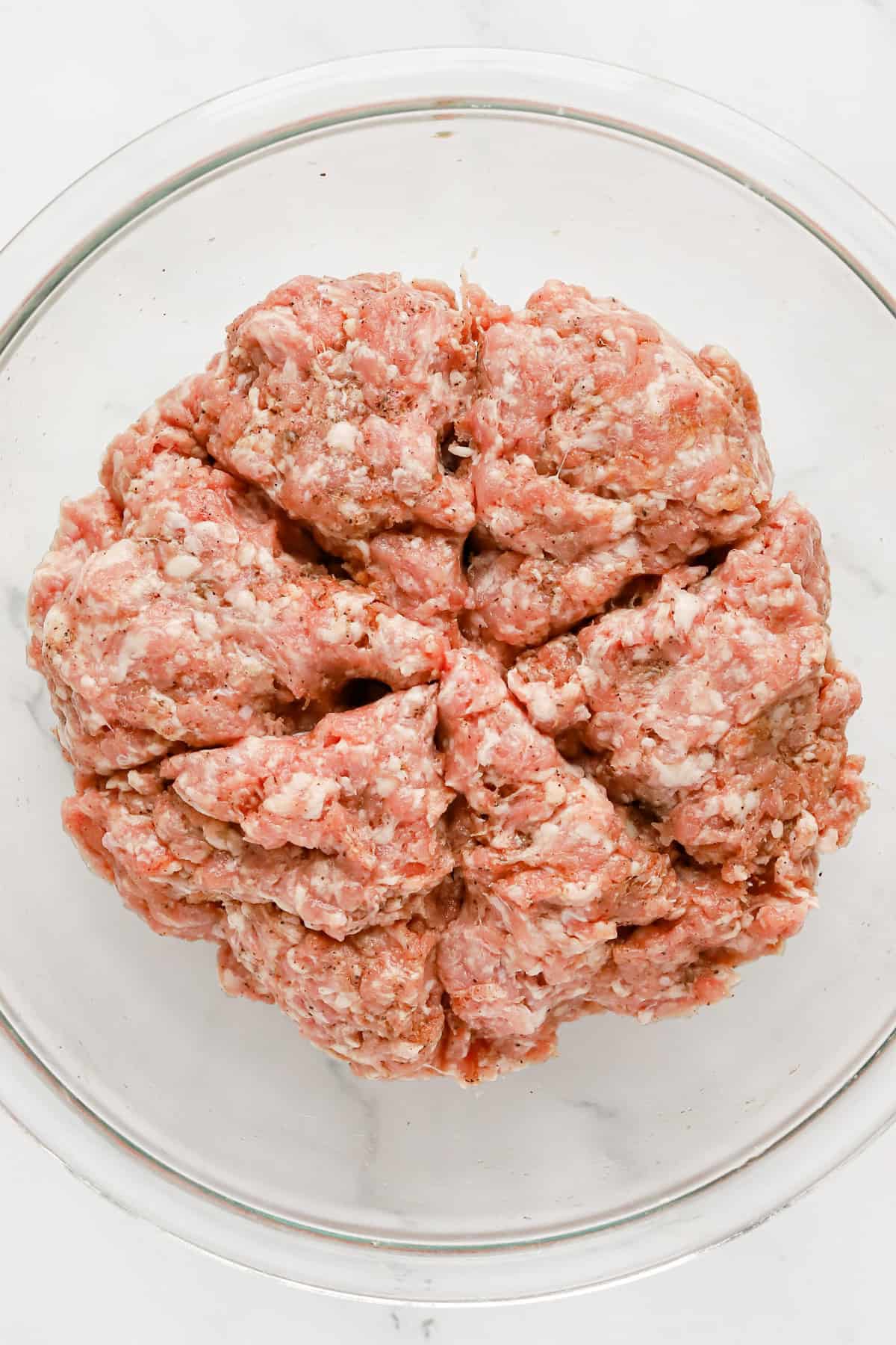 Seasoned pork mixture divided into 6 wedges in a glass bowl.