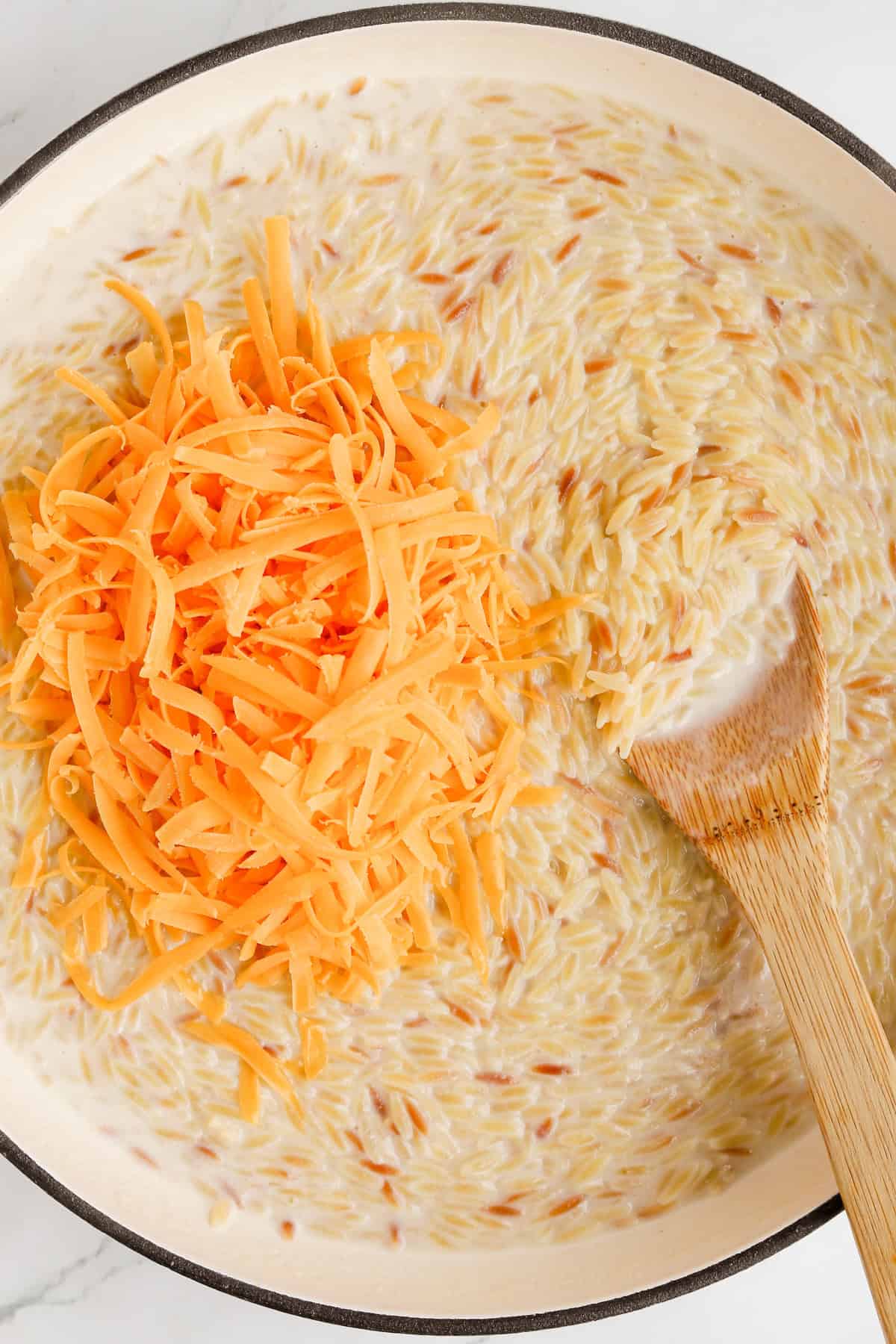 Shredded cheddar cheese added on top of cooked orzo to create creamy cheese sauce.