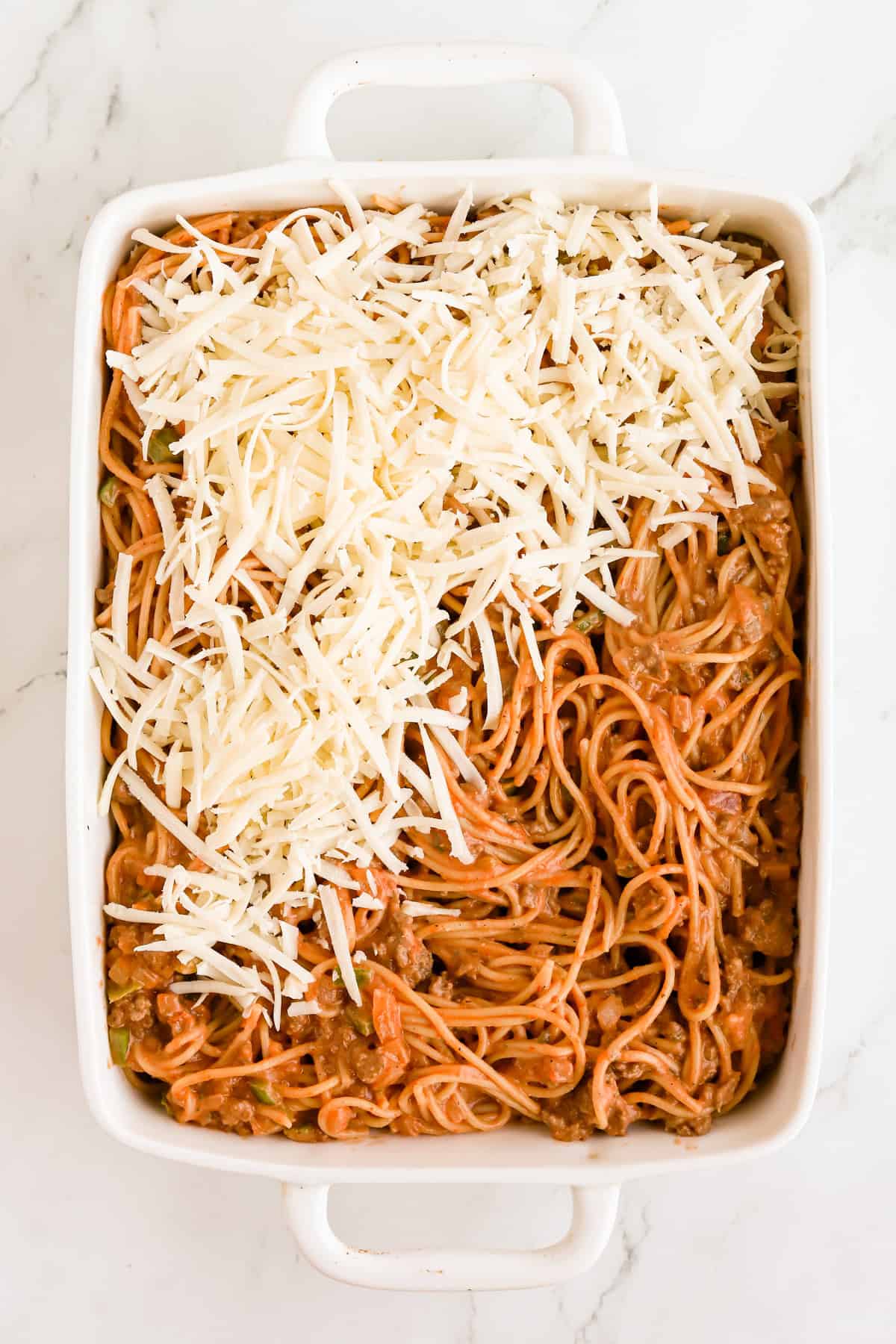 Shredded mozzarella cheese being spread on top of casserole in a white baking dish.