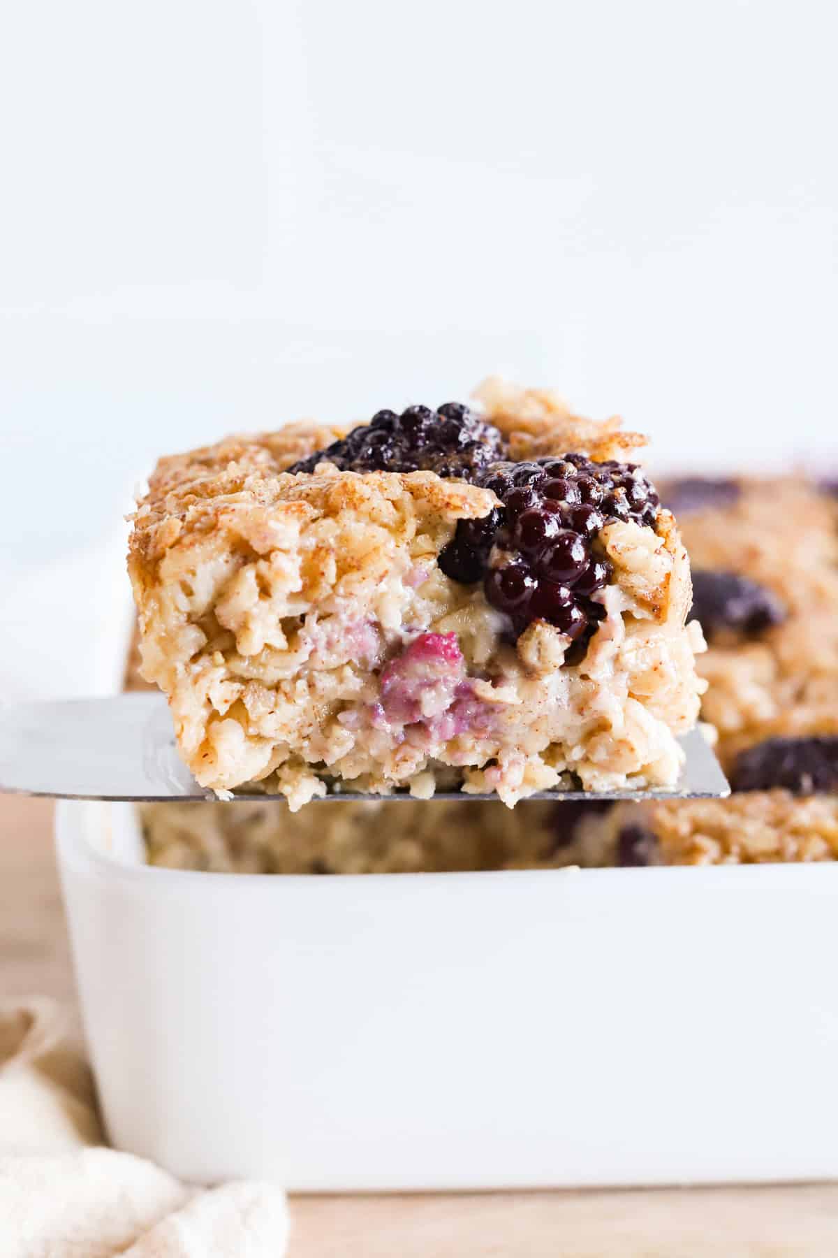 Spatula lifting square of baked oatmeal out of baking dish.