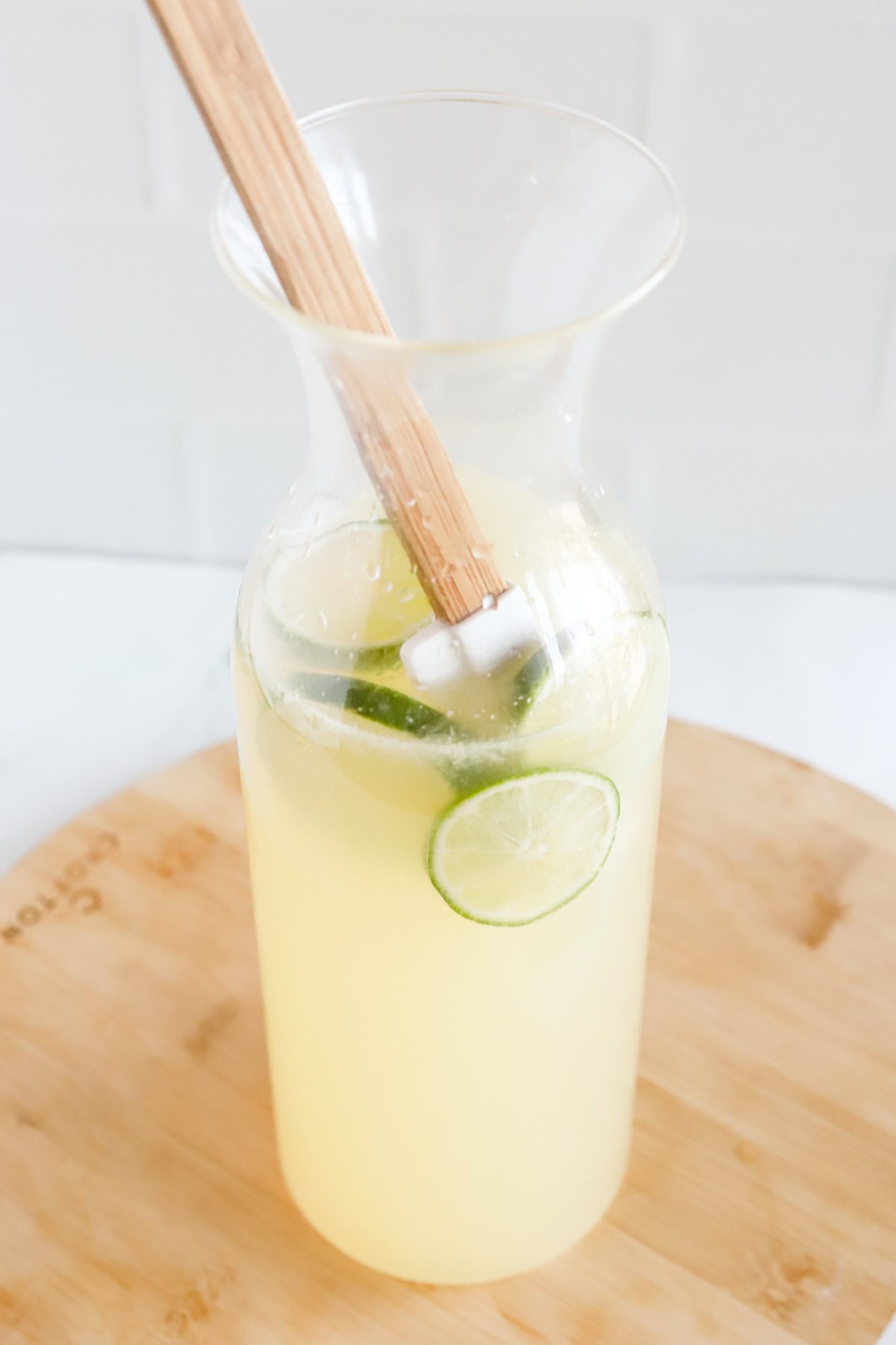 Rubber spatula stirring limeade in glass carafe.