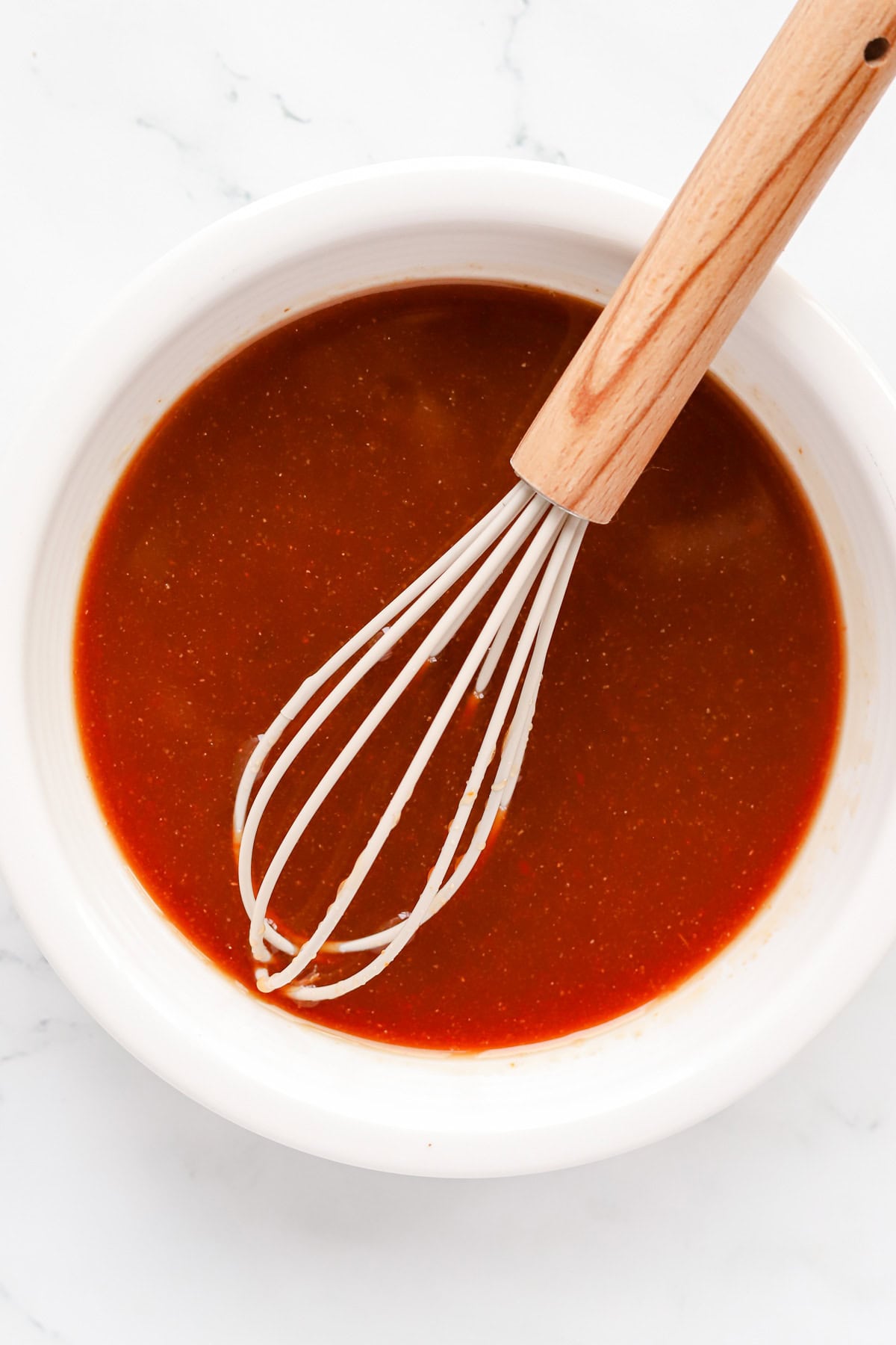 White bowl of homemade sweet and sour sauce with a whisk.