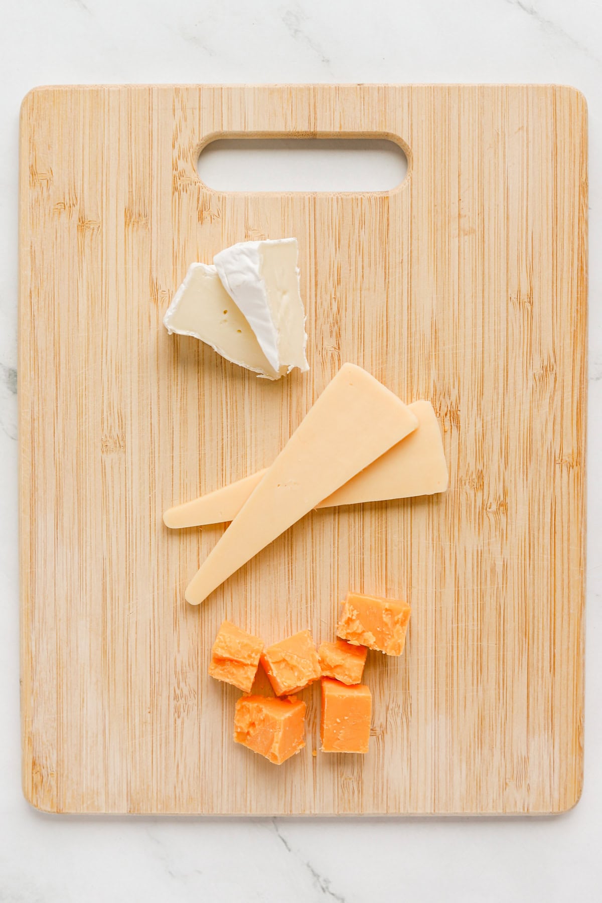 Small Brie wedges, edam cheese and sharp cheddar cheese on a wooden cutting board.