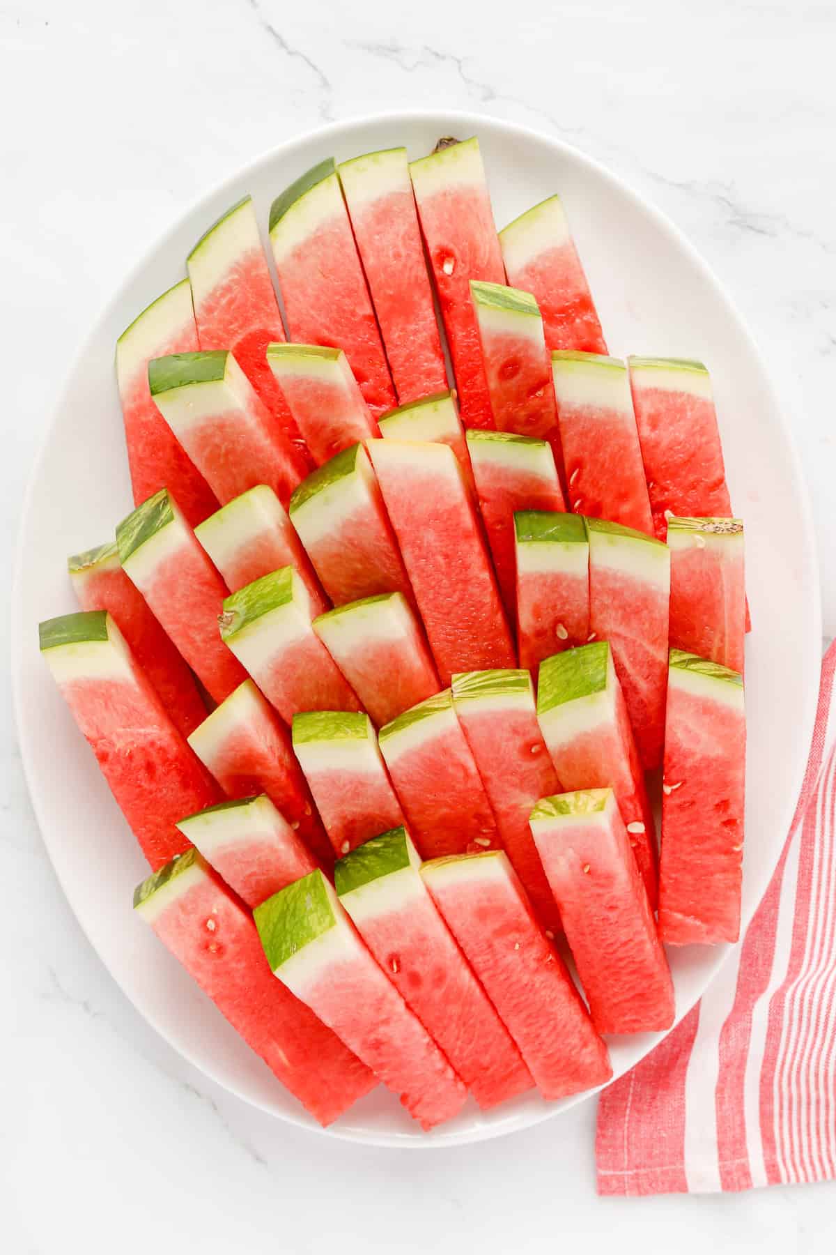 White oval platter of watermelon sticks stacked.
