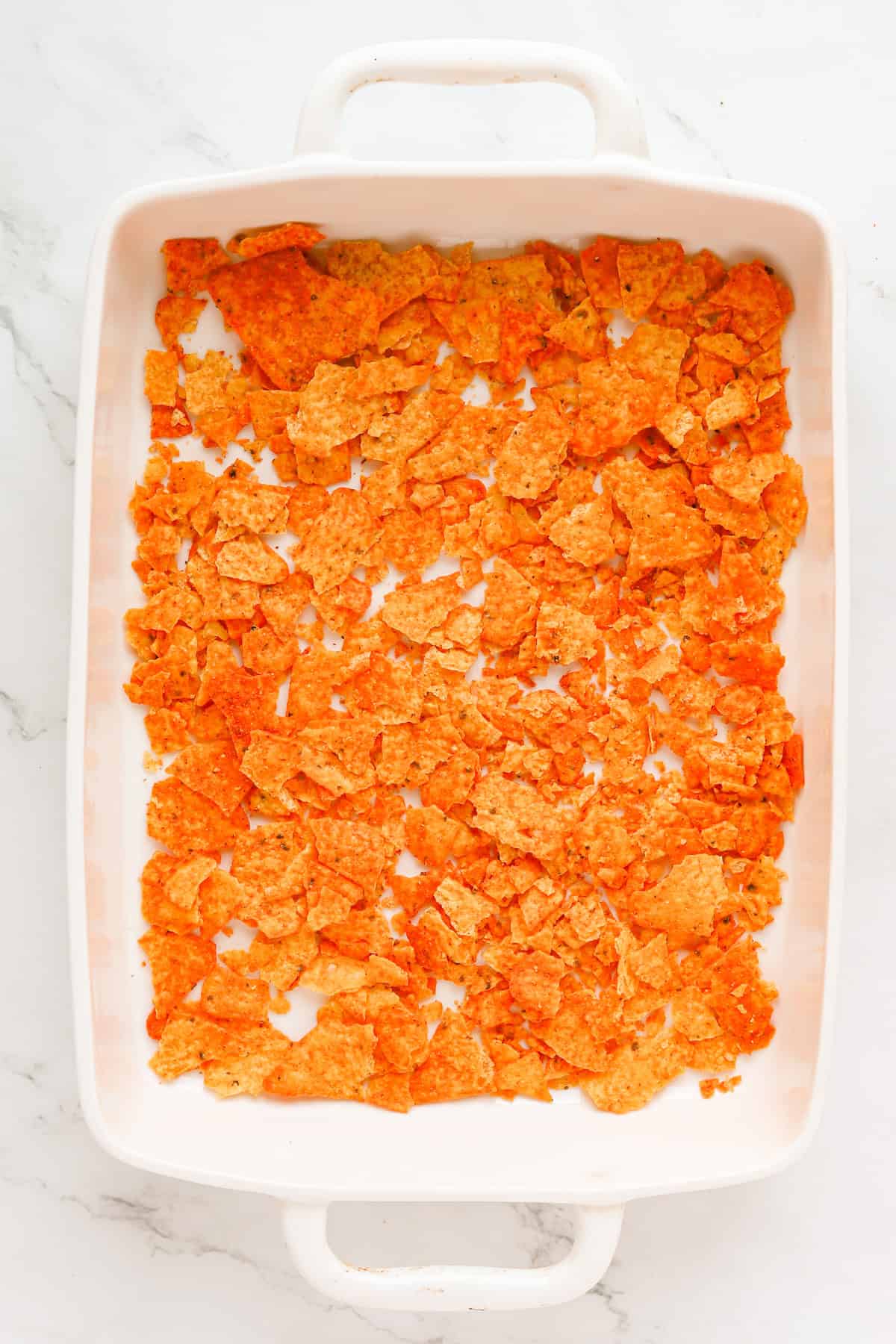 Crushed nacho cheese chips in bottom of 9x13 baking dish.
