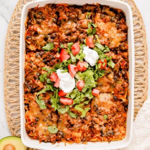 Baked walking taco casserole with shredded romaine, diced tomato and sour cream on top.