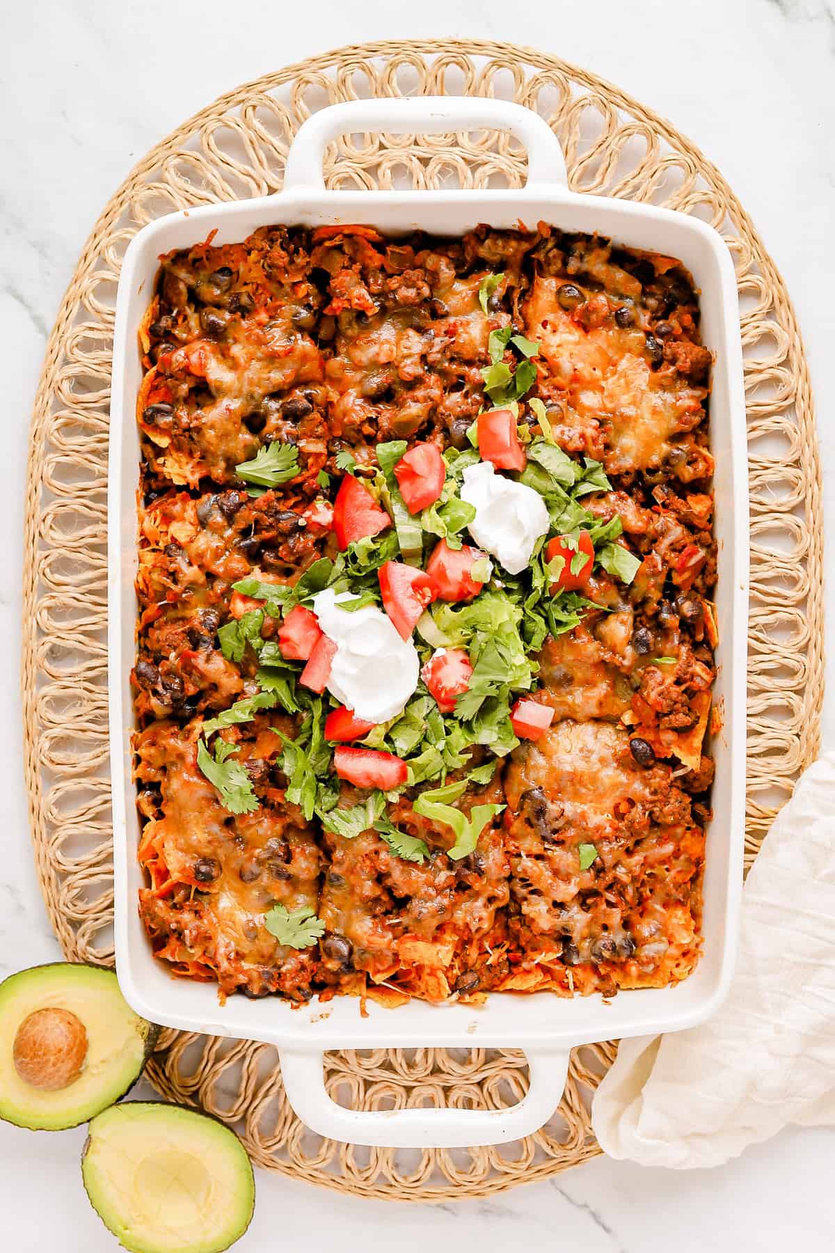 Baked walking taco casserole with shredded romaine, diced tomato and sour cream on top.