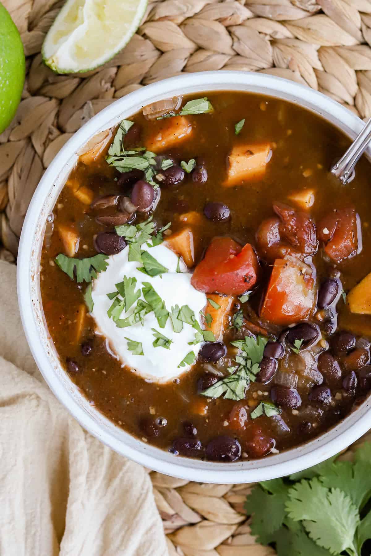 Black bean sweet potato soup garnished with sour cream and chopped cilantro in a bowl.