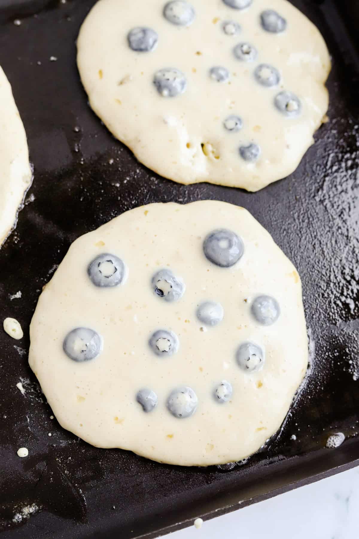 Blueberry pancakes cooking on griddle