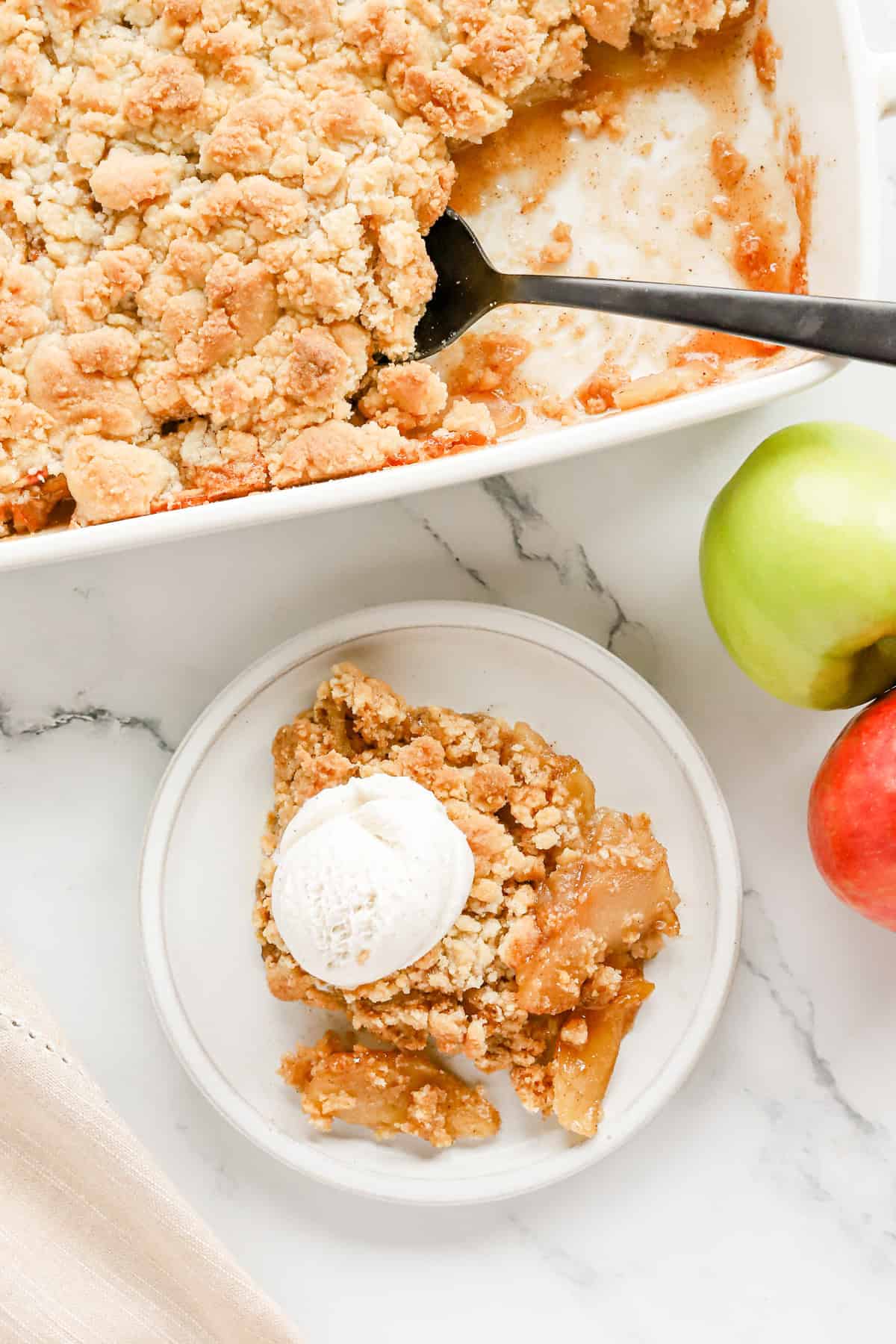 Overhead view of plated apple cobbler with ice cream next to baking dish of cobbler.
