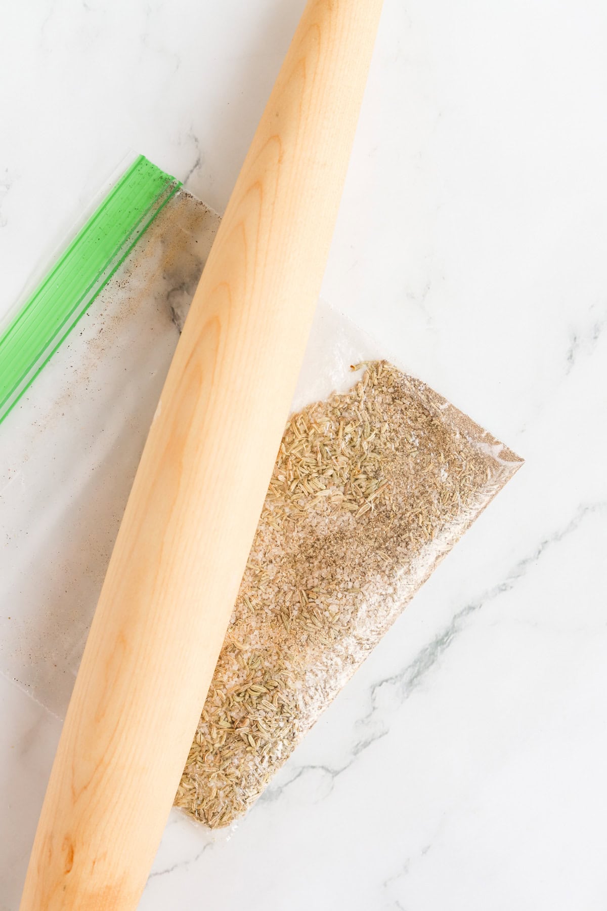 Herbs and spice in zip top bag with a wooden rolling pin on top.