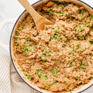 Baked chicken risotto in a ceramic braiser pan with a wooden spoon resting in it.