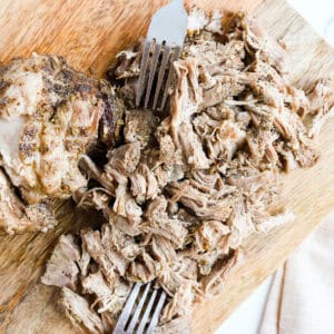 Featured image of shredded porketta roast on wooden cutting board.