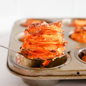 Spoon lifting a potato stack out of the muffin tin.